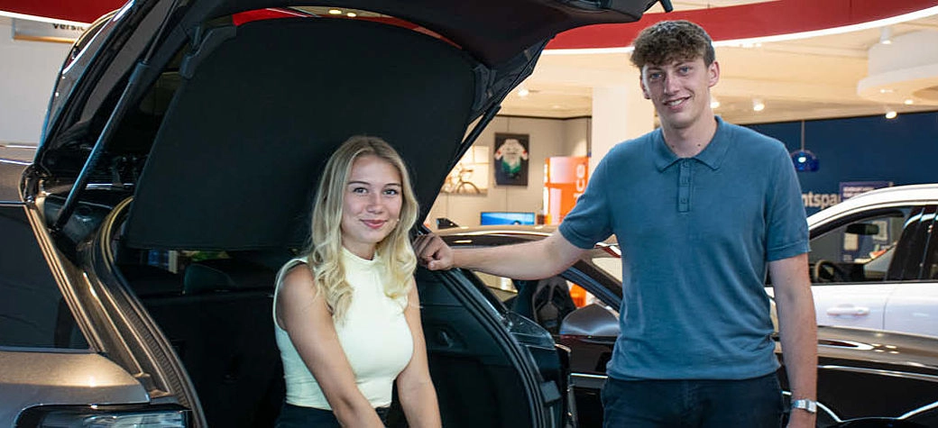 Angelina und Maximilian stehen lächelnd neben einem Auto