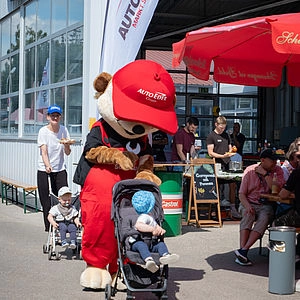 Maskottchen Schraubi schiebt einen Kinderwagen 
