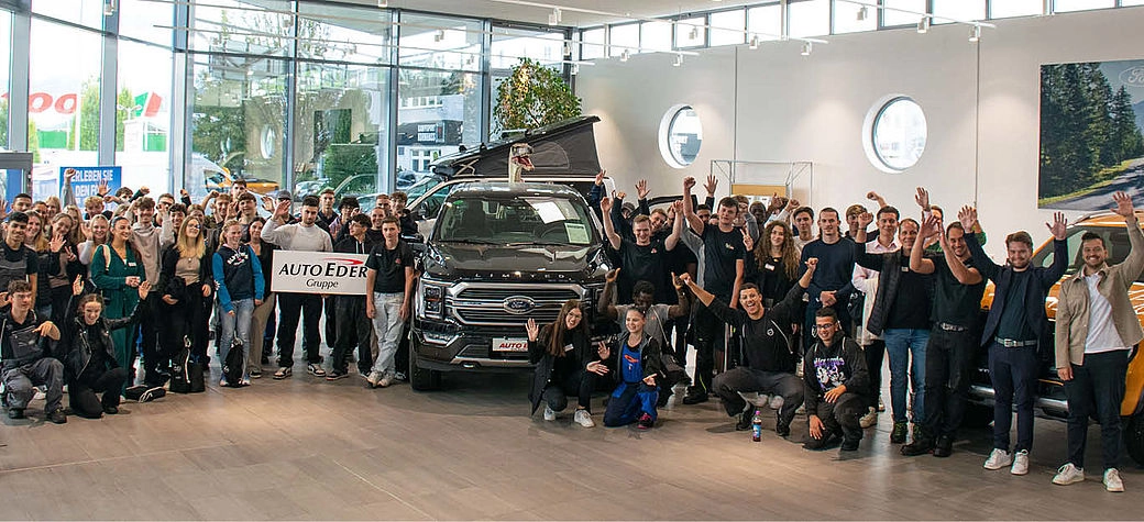 Alle neuen Azubis aufgestellt neben einem Auto